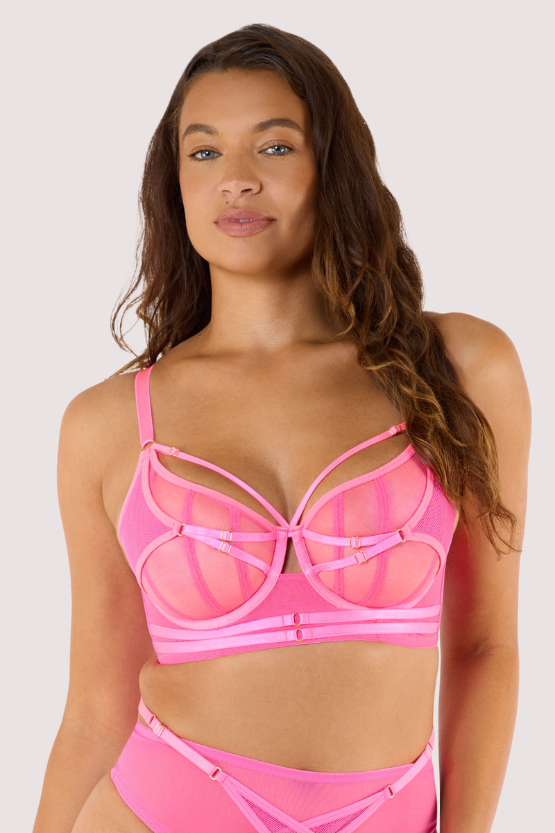 Model wears neon pink balconette bra with strappy details and sheer mesh panels, showcasing a bold design.
