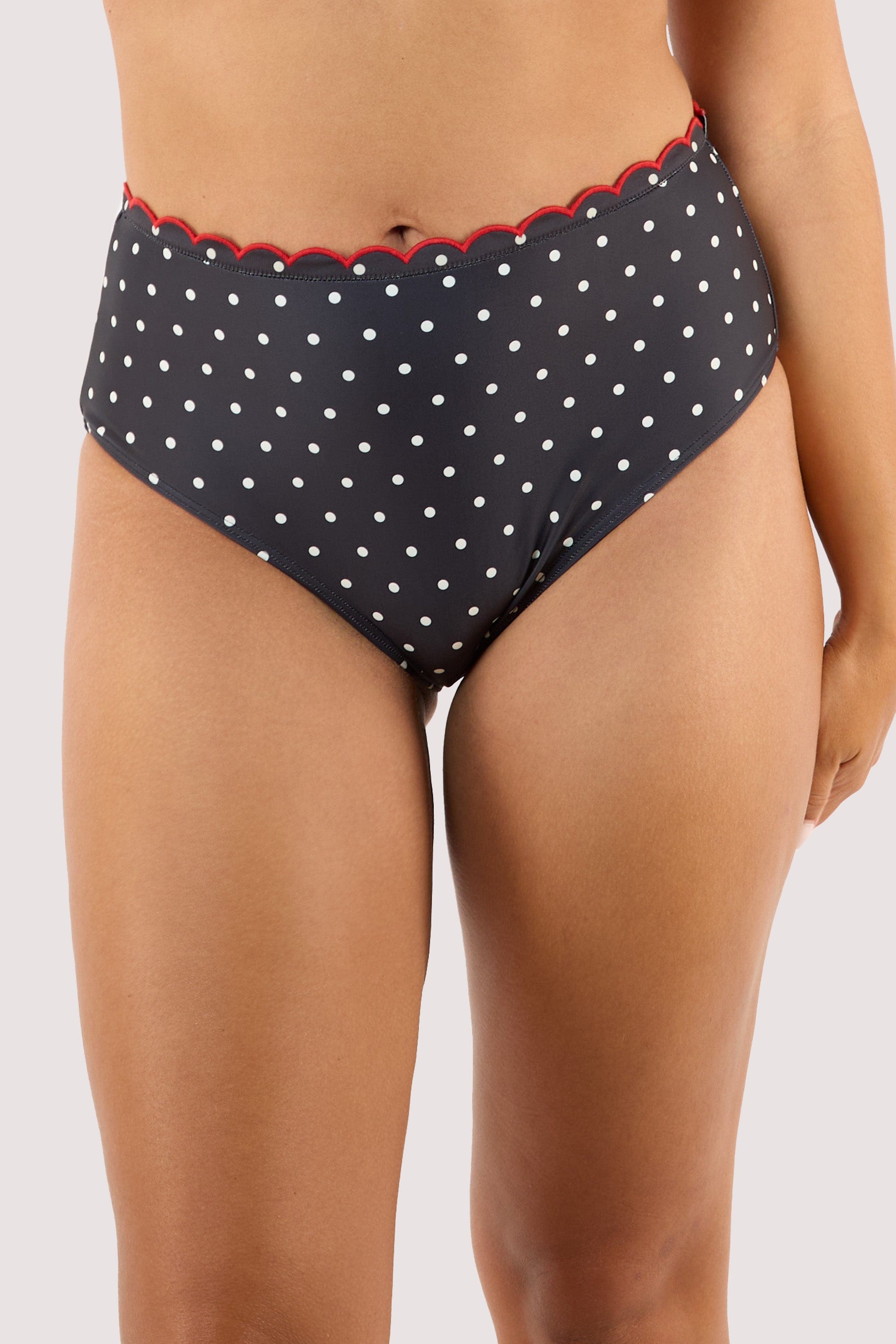 Model Wearing a playful black and white polka dot bikini with red scallops, highlighting a retro high-waist style.