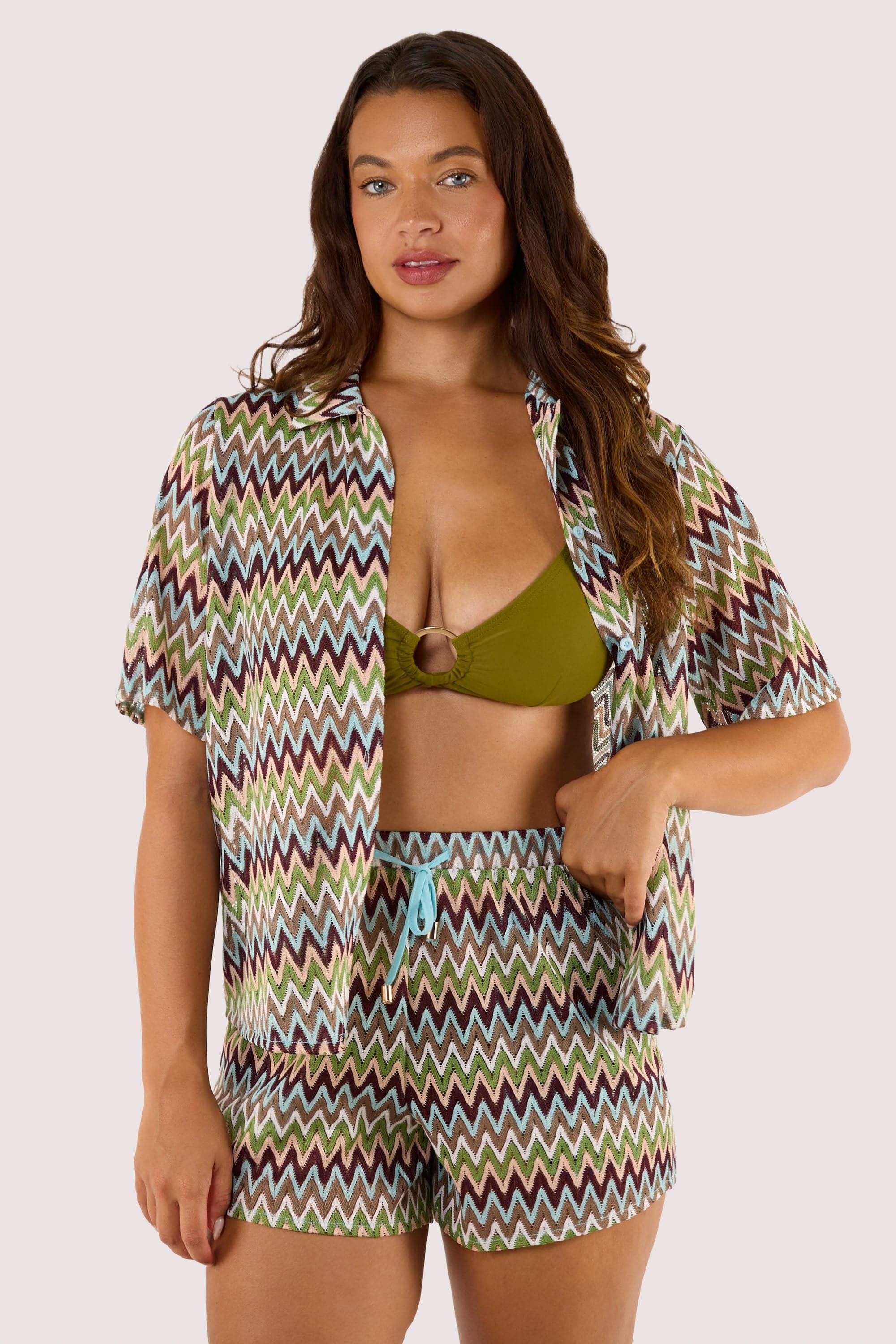 Model Wearing green bikini top and shorts, complemented by a breezy crochet beach shirt with a button-down front and zig-zag pattern.
