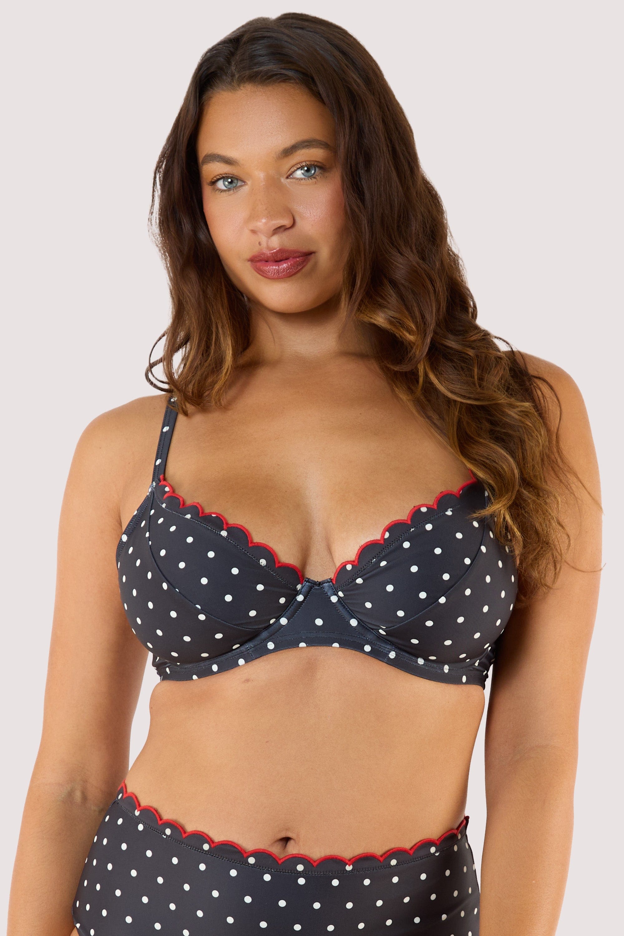 model Wearing a black polka dot bikini top with red scalloped edges, showcasing supportive underwired cups and adjustable straps.