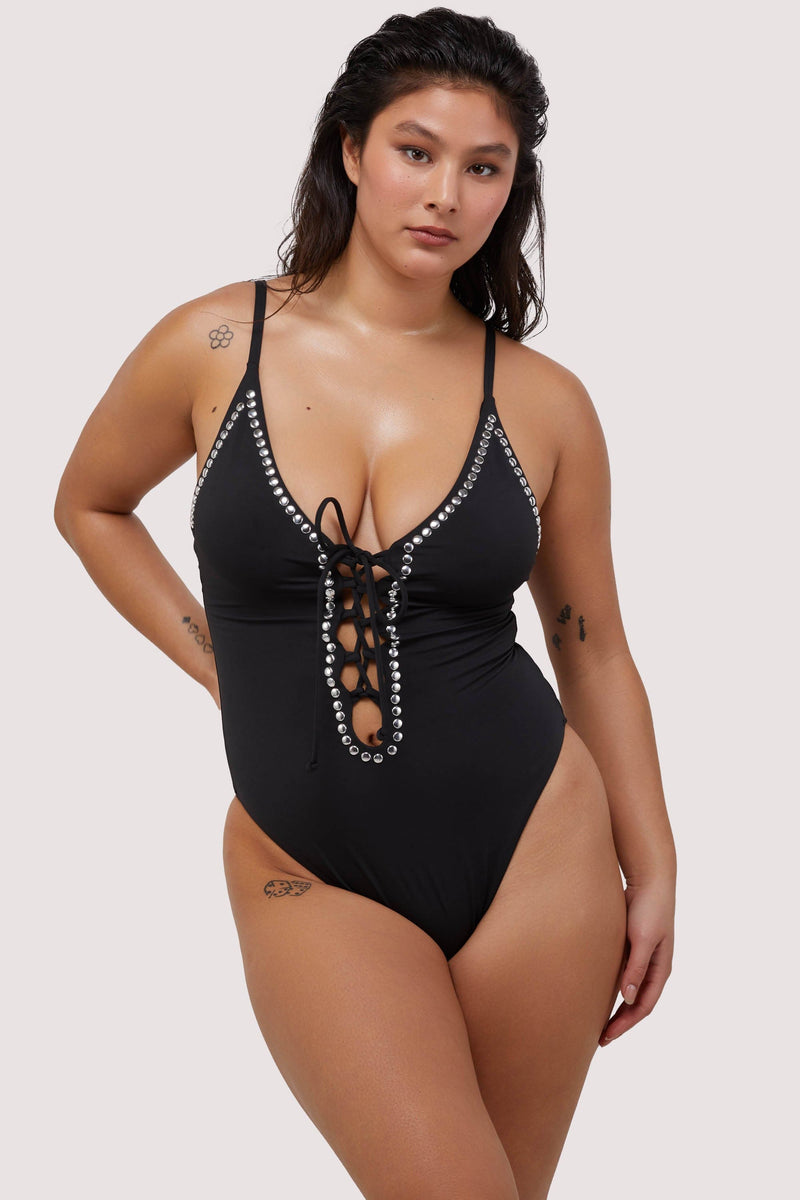 Model wears black plunge neckline lace-up swimsuit with silver studs