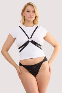 Model wears a black elastic body harness with adjustable straps and gold hardware over a white crop top.