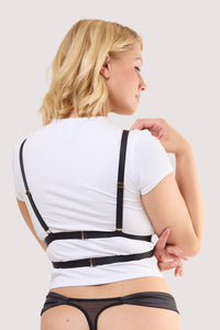Model wears a black elastic body harness with adjustable straps and gold hardware over a white crop top.