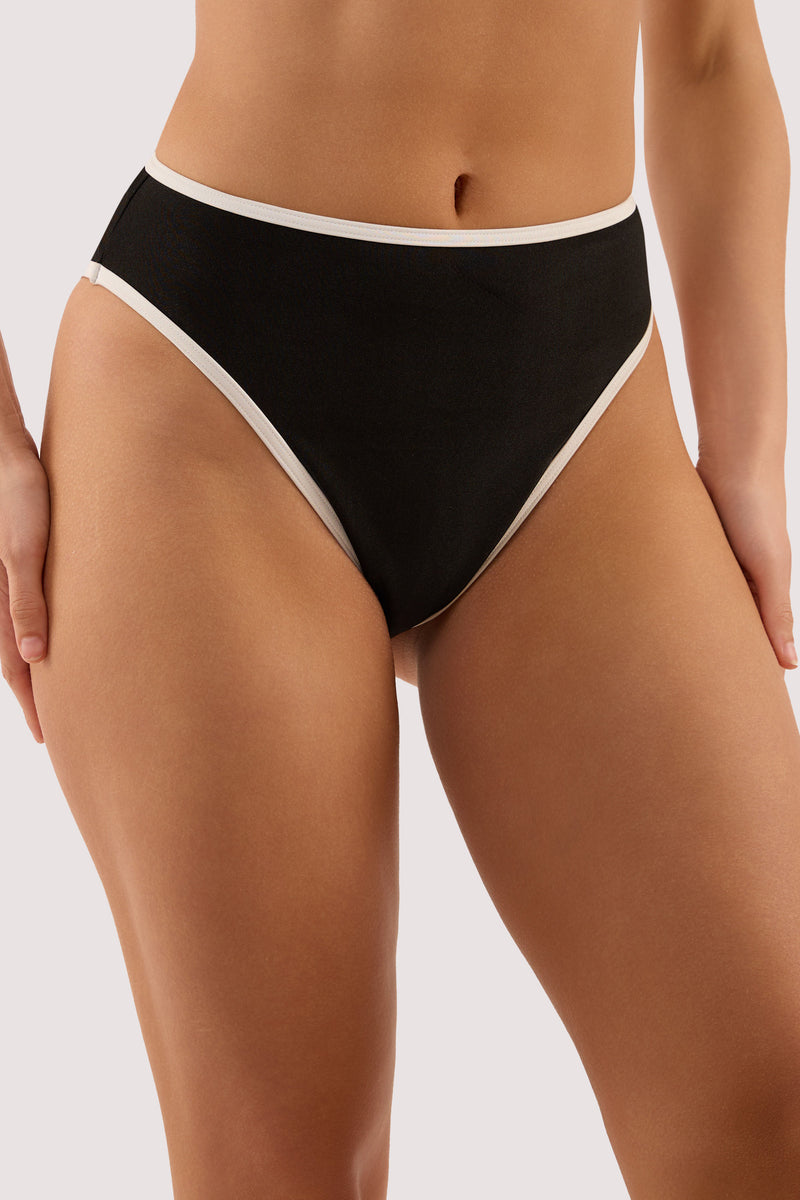 Model wears a ally black & ivory high waist bikini brief with tanga and high waist, high-leg style featuring ivory contrast trim.