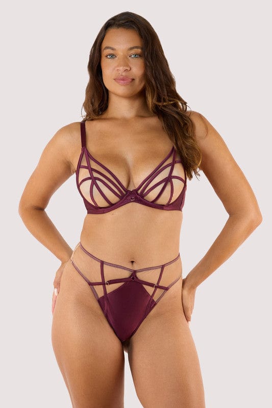Model wears a wine high waist thong featuring a satin central panel, strap detailing, and gold metal hardware with a matching wine plunge bra.