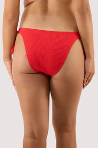 Model Back view of red textured bikini bottoms in a cheeky cut, worn by a woman, showing the snug fit and ribbed fabric detail.