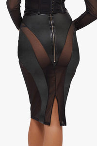 Model shows the back of a black vegan leather mesh insert pencil skirt with gold zip detail and below the knee cut with back split.